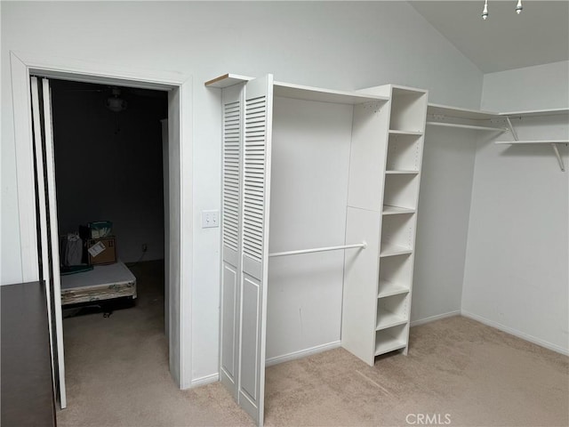 walk in closet with vaulted ceiling and light colored carpet