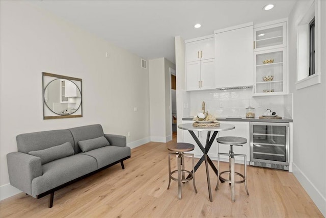 interior space with white cabinets, light hardwood / wood-style floors, decorative backsplash, beverage cooler, and a breakfast bar