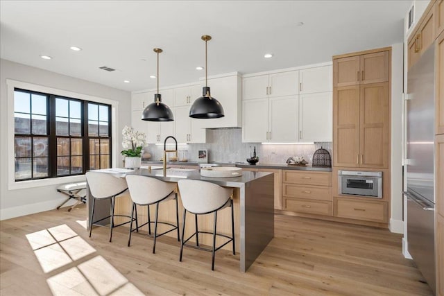 kitchen featuring a kitchen island with sink, hanging light fixtures, light wood-type flooring, white cabinets, and sink