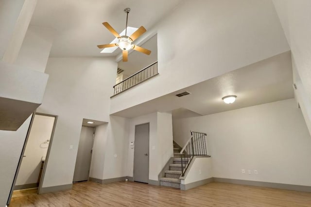 unfurnished living room with ceiling fan, light hardwood / wood-style flooring, and a towering ceiling