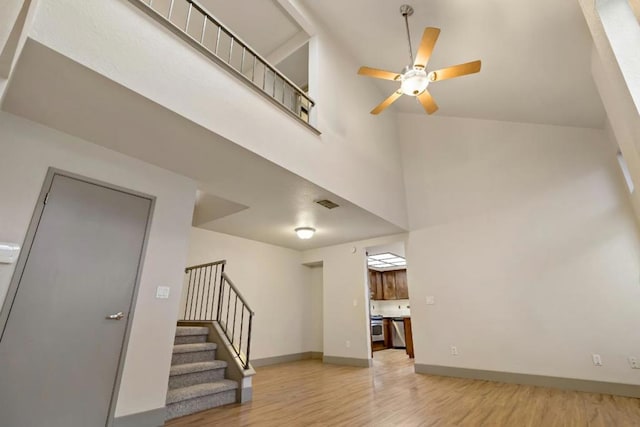 unfurnished living room with a towering ceiling, ceiling fan, and light hardwood / wood-style flooring