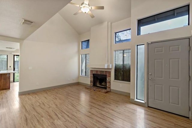 unfurnished living room featuring ceiling fan, light hardwood / wood-style floors, a brick fireplace, and high vaulted ceiling