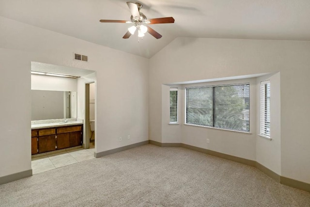 unfurnished bedroom featuring ceiling fan, light colored carpet, ensuite bath, and lofted ceiling