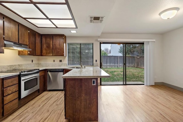 kitchen with light hardwood / wood-style floors, stainless steel appliances, a center island, light stone countertops, and sink