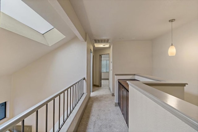 hallway featuring lofted ceiling with skylight and light colored carpet