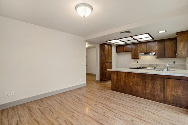 kitchen with kitchen peninsula, light hardwood / wood-style floors, dark brown cabinets, and sink