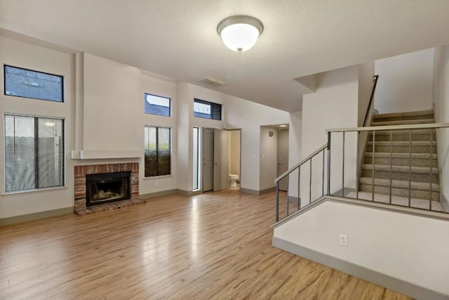 living room featuring a brick fireplace, a textured ceiling, and light hardwood / wood-style floors