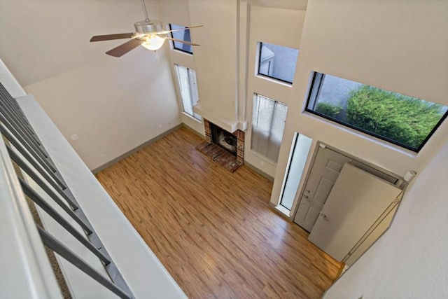 foyer entrance with a towering ceiling, wood-type flooring, a brick fireplace, and ceiling fan