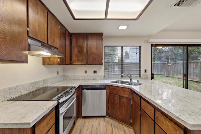 kitchen featuring stainless steel appliances, sink, light stone counters, light wood-type flooring, and kitchen peninsula