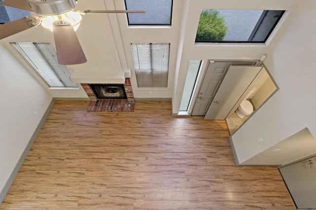 foyer with ceiling fan, light hardwood / wood-style flooring, a fireplace, and a high ceiling