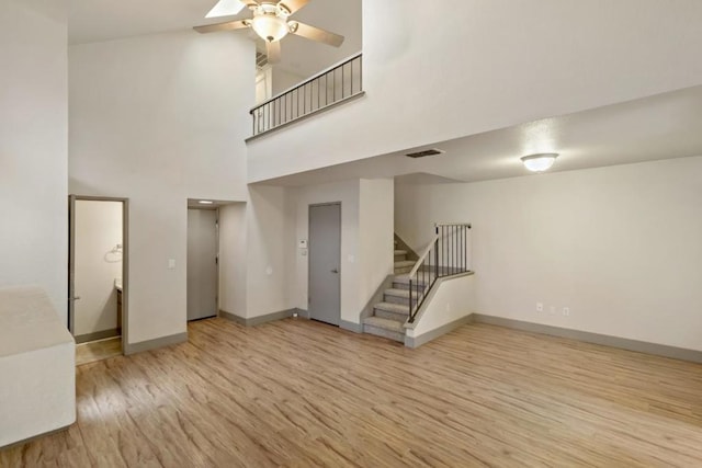 unfurnished living room with a high ceiling, ceiling fan, and light hardwood / wood-style flooring