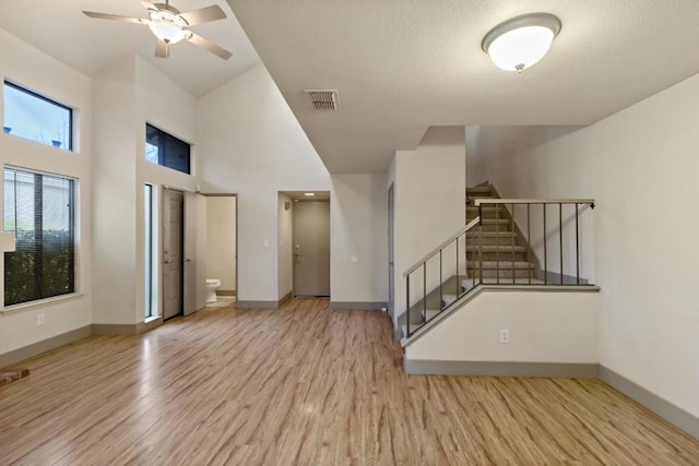 unfurnished living room featuring a high ceiling, ceiling fan, and light hardwood / wood-style flooring