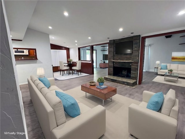 living room featuring lofted ceiling, a large fireplace, and light wood-type flooring