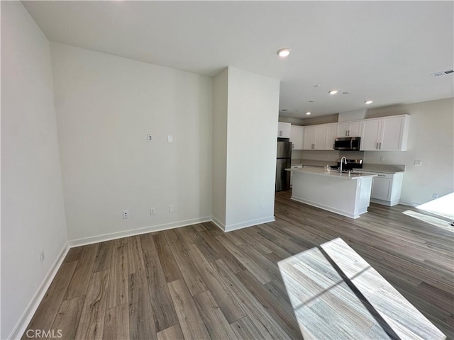 kitchen with white cabinets, stainless steel appliances, sink, hardwood / wood-style flooring, and a center island with sink