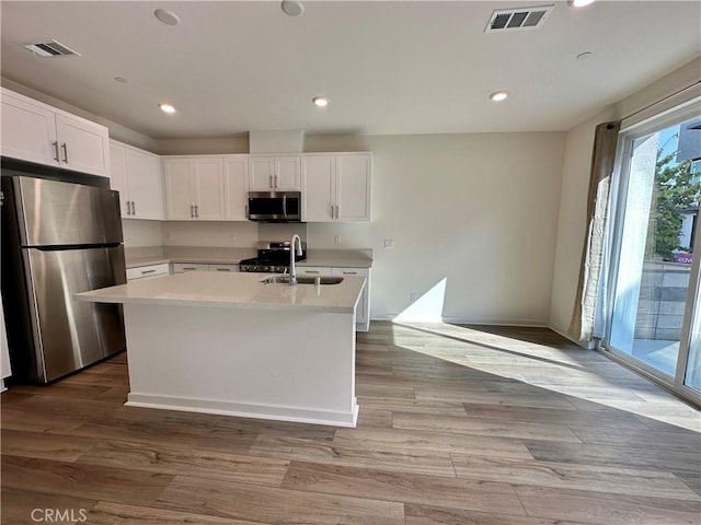 kitchen featuring white cabinetry, a center island with sink, appliances with stainless steel finishes, light hardwood / wood-style flooring, and sink