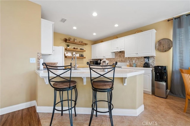 kitchen with kitchen peninsula, a breakfast bar, sink, white cabinetry, and light tile patterned flooring