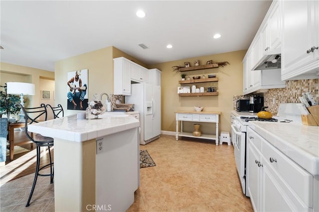 kitchen with white appliances, tile counters, white cabinets, a kitchen breakfast bar, and sink