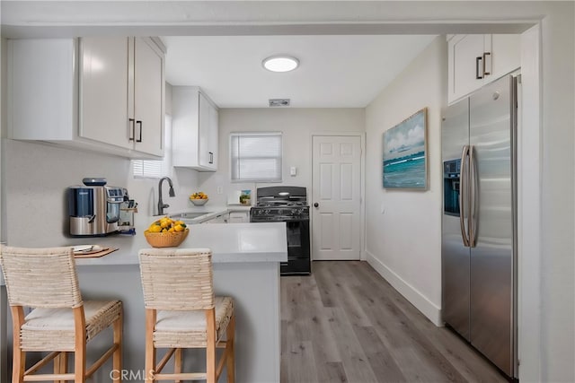 kitchen with kitchen peninsula, a kitchen breakfast bar, black gas stove, and stainless steel fridge