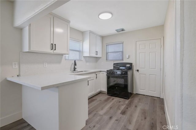 kitchen featuring kitchen peninsula, light hardwood / wood-style floors, white cabinetry, black gas range, and sink