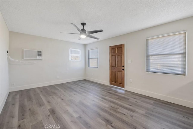 unfurnished room with a textured ceiling, ceiling fan, hardwood / wood-style floors, and an AC wall unit