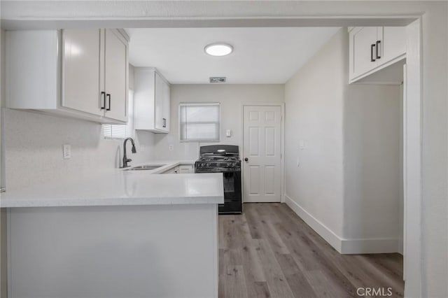 kitchen featuring black gas range, light hardwood / wood-style floors, kitchen peninsula, sink, and white cabinetry