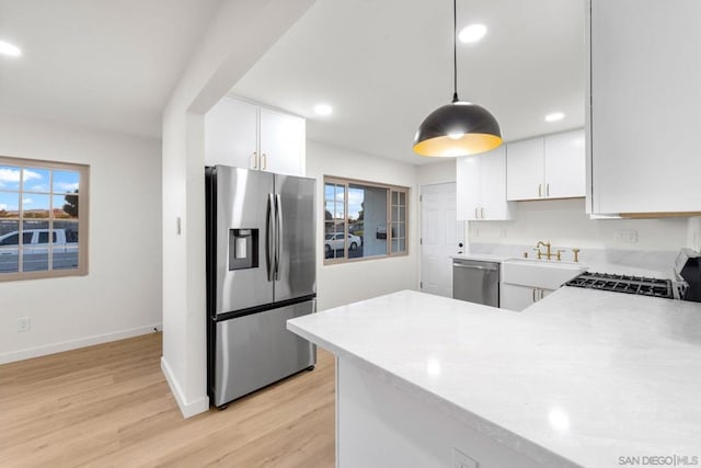 kitchen with light wood-type flooring, appliances with stainless steel finishes, white cabinetry, and pendant lighting