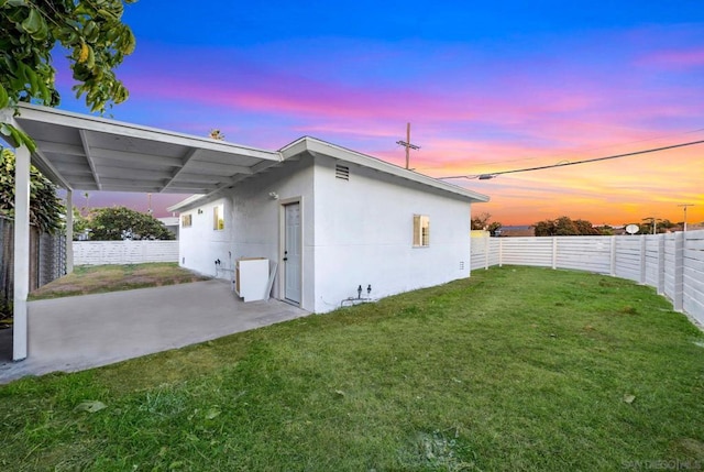 back house at dusk with a lawn and a patio