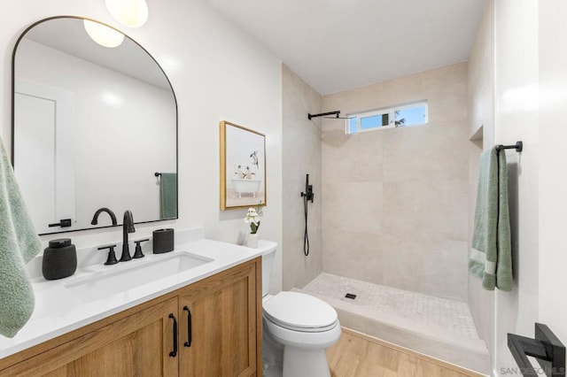 bathroom with hardwood / wood-style floors, toilet, vanity, and tiled shower