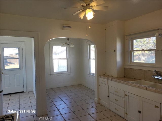 kitchen featuring sink, white cabinets, tile countertops, light tile patterned floors, and ceiling fan with notable chandelier