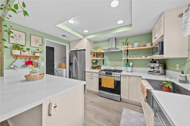 kitchen with a raised ceiling, appliances with stainless steel finishes, wall chimney exhaust hood, and white cabinetry