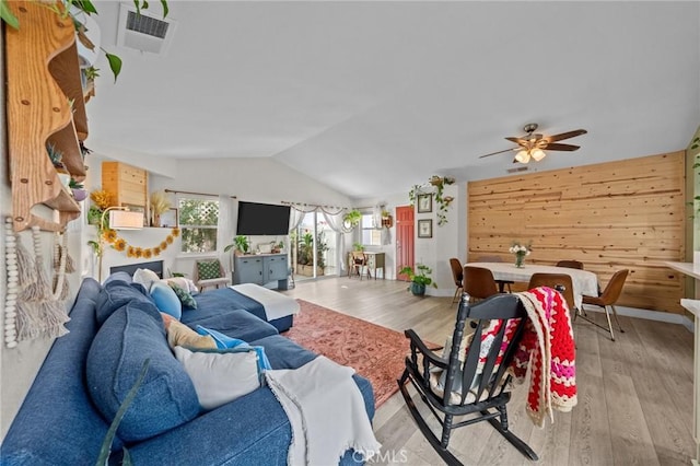 living room featuring vaulted ceiling, ceiling fan, wood walls, and light hardwood / wood-style floors