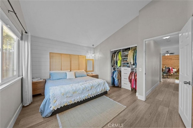 bedroom featuring light hardwood / wood-style flooring, wooden walls, a closet, and lofted ceiling