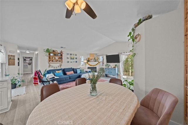 dining space with ceiling fan, light hardwood / wood-style floors, lofted ceiling, and a fireplace