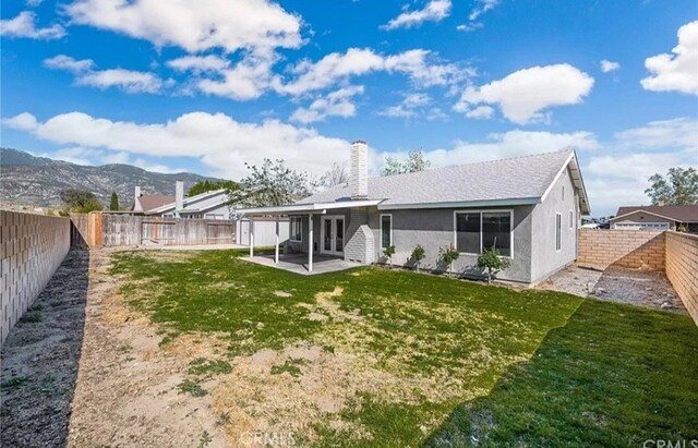 back of house with a lawn, a mountain view, and a patio area