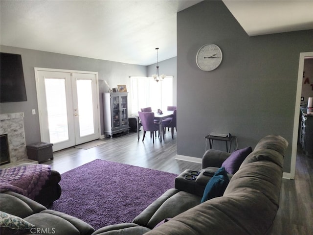 living room featuring french doors, a notable chandelier, lofted ceiling, a fireplace, and wood-type flooring