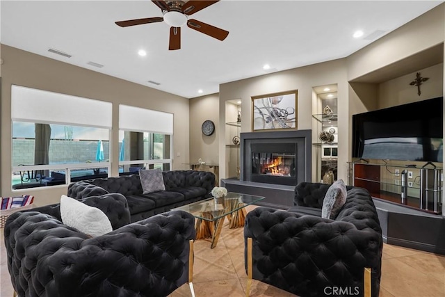 living room with built in shelves, ceiling fan, and light tile patterned floors