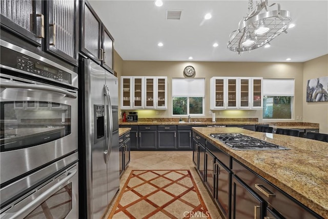 kitchen with light stone counters, hanging light fixtures, stainless steel appliances, light tile patterned floors, and dark brown cabinets