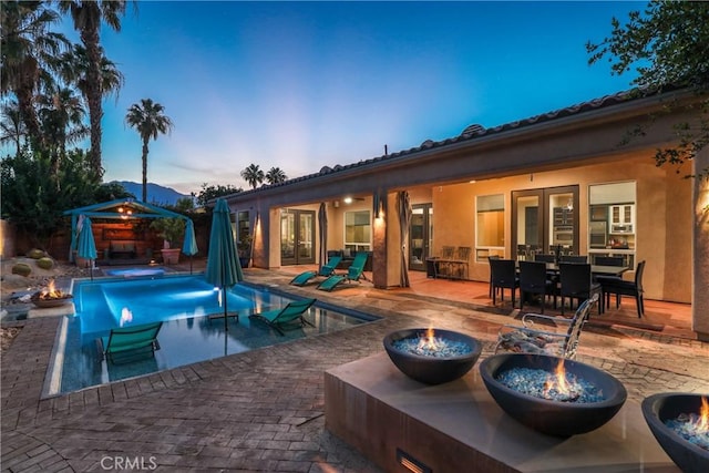 pool at dusk featuring a gazebo, pool water feature, a fire pit, and a patio area