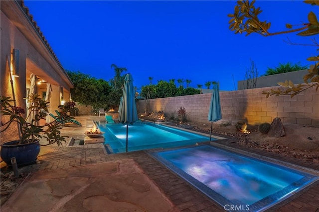 pool at twilight featuring a fire pit, an in ground hot tub, and a patio area