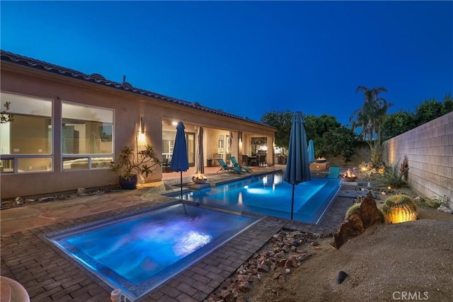 pool at night with a patio and an in ground hot tub