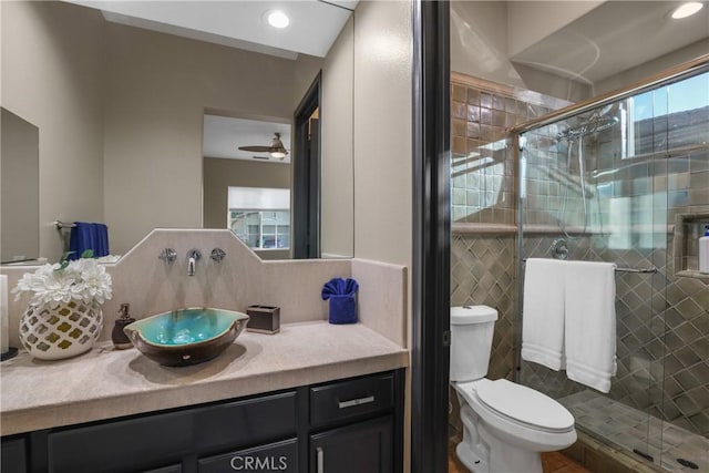 bathroom featuring toilet, plenty of natural light, ceiling fan, a shower with shower door, and vanity