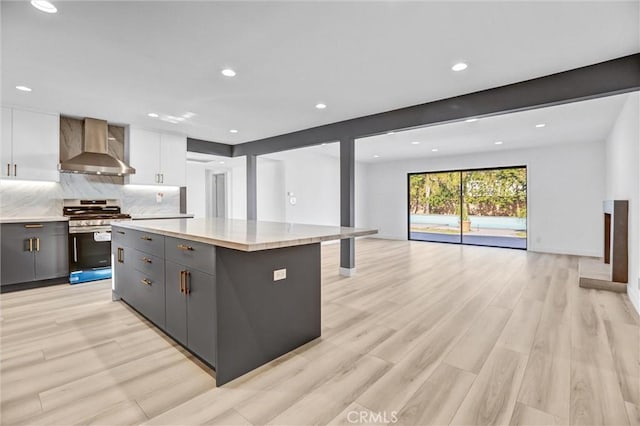 kitchen with a kitchen island, white cabinetry, wall chimney range hood, gray cabinets, and stainless steel gas range oven