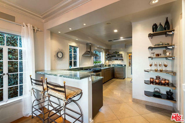 kitchen with sink, a kitchen bar, dark stone countertops, kitchen peninsula, and range hood