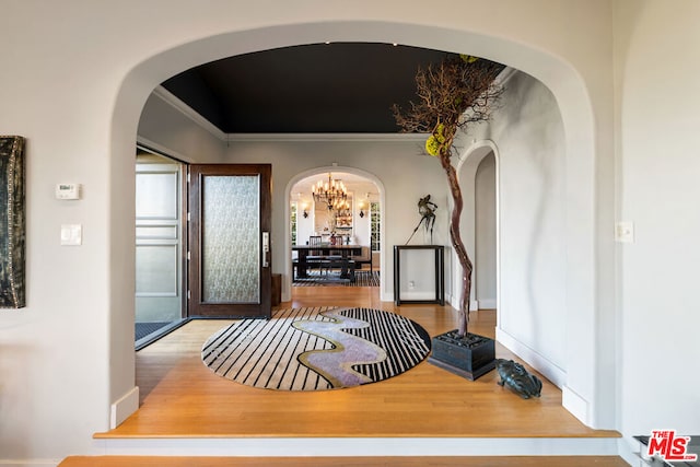 corridor featuring a notable chandelier, light hardwood / wood-style floors, and ornamental molding