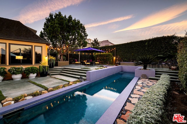 pool at dusk featuring a patio