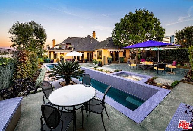 pool at dusk featuring an outdoor hangout area, a patio, and an in ground hot tub