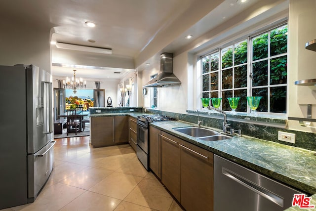 kitchen featuring sink, wall chimney exhaust hood, dark stone counters, pendant lighting, and appliances with stainless steel finishes