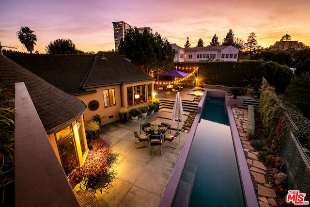 pool at dusk with a fire pit and a patio