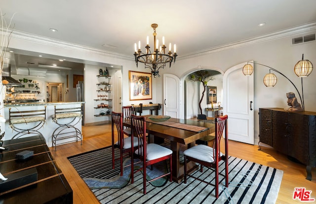 dining space featuring ornamental molding, light wood-type flooring, and a notable chandelier