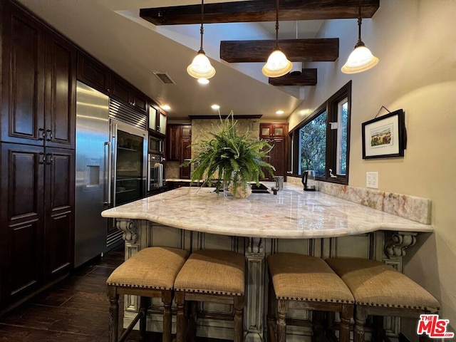 kitchen featuring a breakfast bar, hanging light fixtures, built in fridge, and dark brown cabinetry